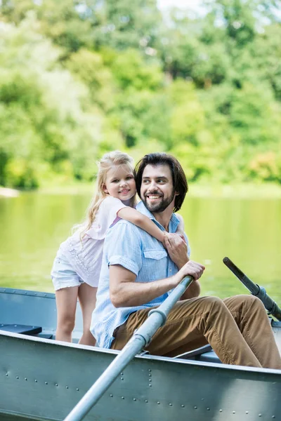 微笑的女儿拥抱父亲从后面 当他们乘坐小船在湖在公园 — 图库照片