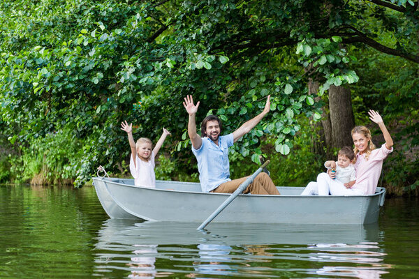 happy young family with raised hands riding boat on lake at park