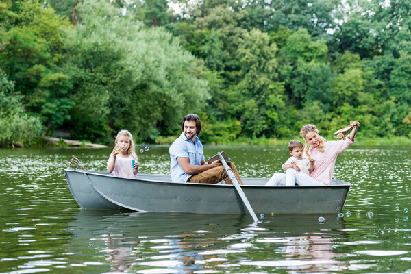 smiling young family spending time together in boat on lake at park