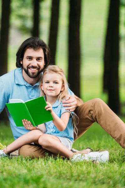 Feliz Padre Hija Leyendo Libro Mientras Está Sentado Hierba Parque —  Fotos de Stock