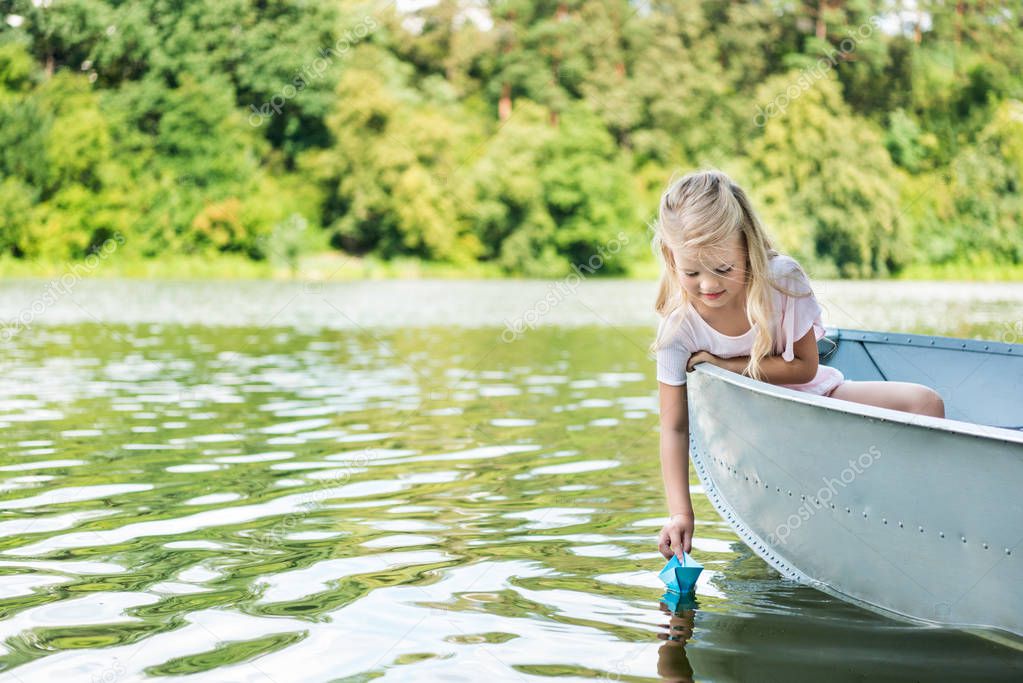 happy little child launching paper origami boat while floating in boat on lake
