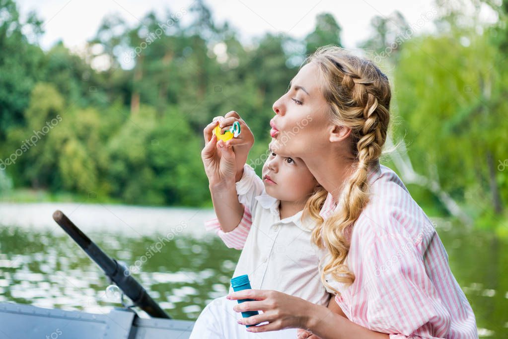 happy mother with son blowing soap bubbles while riding boat at park