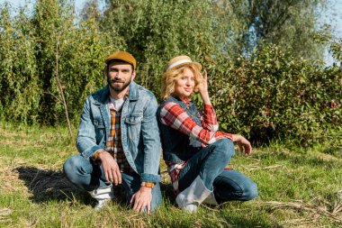 kameraya bakarak ve açık havada çimenlerin üzerinde oturan çift 