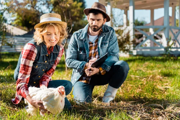 选择焦点的妇女抱着鸡 而她的男朋友写在剪贴板在农场 — 图库照片