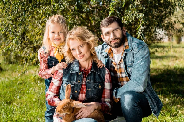 成年农民家庭与女儿和棕色兔子坐在草地上户外 — 免费的图库照片