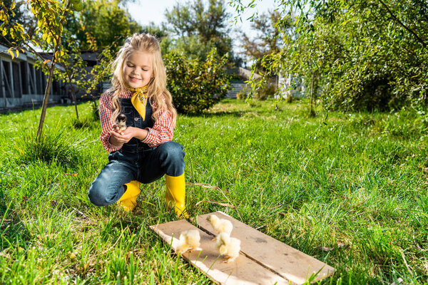 happy child sitting on grass near yellow baby chicks at farm