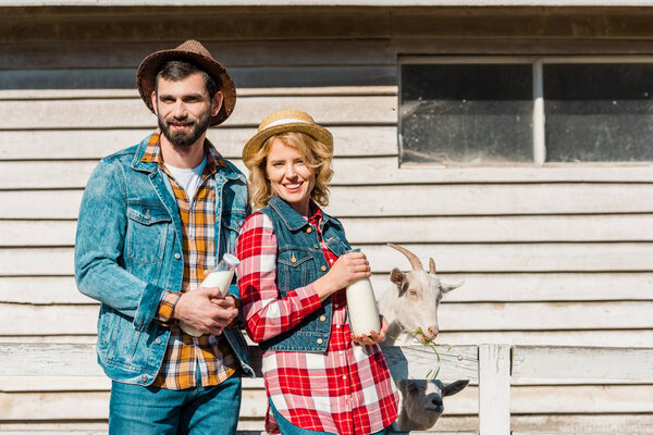 farmers holding bottles of milk while goat standing near wooden fence at ranch