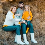 Hermosa mujer vertiendo leche en el vaso mientras su marido y su hija se sientan cerca de la granja