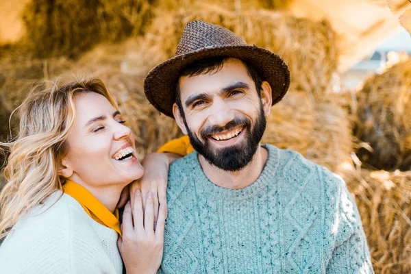 農家の農場で干し草のスタックの上に座ってのカップルを笑う — ストック写真