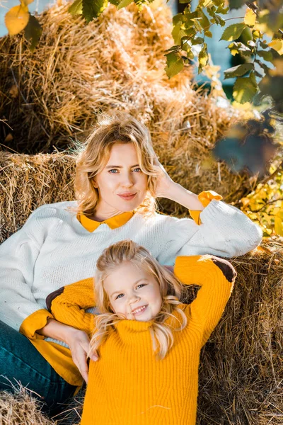 Schöne Bäuerin Posiert Mit Kleiner Tochter Auf Heuhaufen Auf Ranch Stockfoto