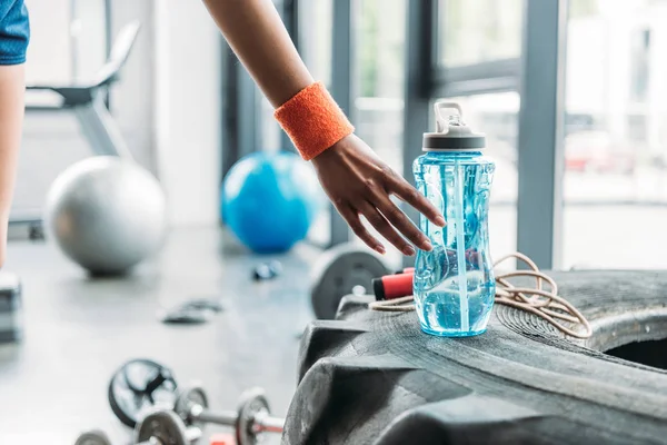 Cropped image of sportswoman in wristband picking up bottle of water from training tire at gym — Stock Photo