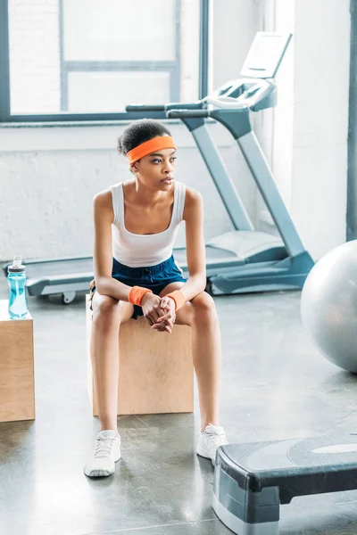 Afrikanisch-amerikanische Sportlerin mit Stirnband und Stirnbändern ruht auf Holzkiste im Fitnessstudio — Stockfoto