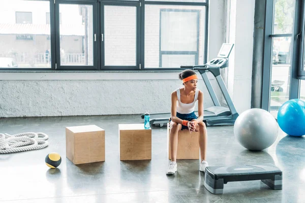 Young female athlete sitting on wooden box at gym — Stock Photo