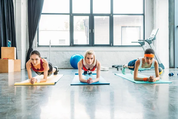 Вид спереду багатоетнічних спортсменів, які роблять дошку на фітнес-матів у спортзалі — стокове фото