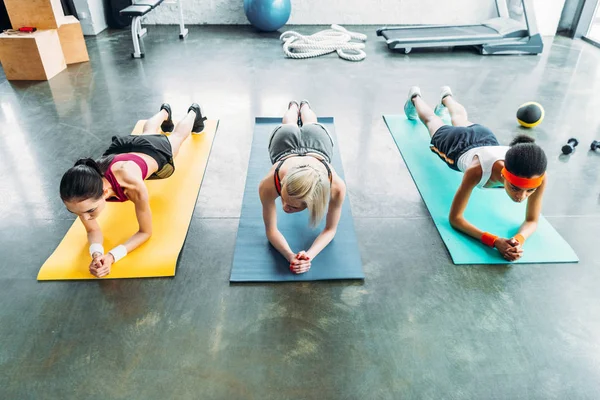 Drei junge multikulturelle Sportlerinnen beim Planken im Fitnessstudio — Stockfoto