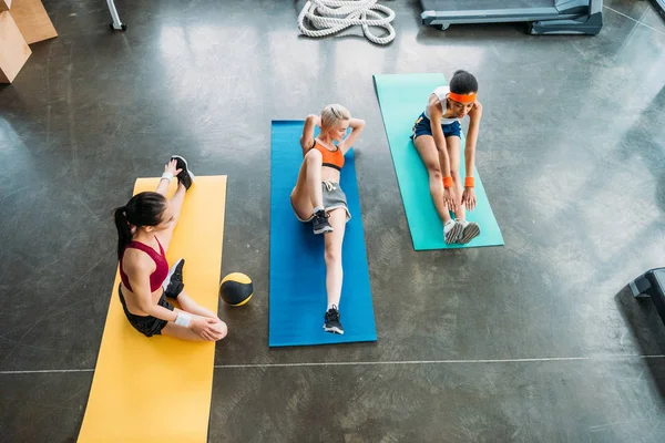 Vista ad alto angolo di tre sportivi multietnici che si esercitano su tappeti fitness in palestra — Foto stock