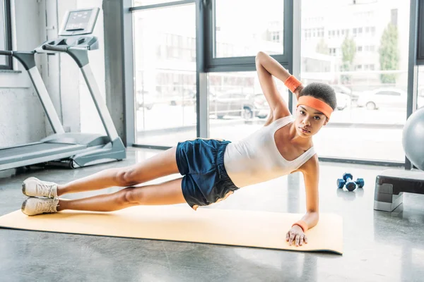 Africaine américaine sportive faisant planche latérale de tapis de fitness à la salle de gym — Photo de stock