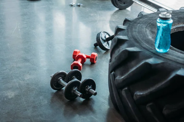 Diferentes halteres, rolo abs e garrafa de água no pneu de treinamento no ginásio — Fotografia de Stock