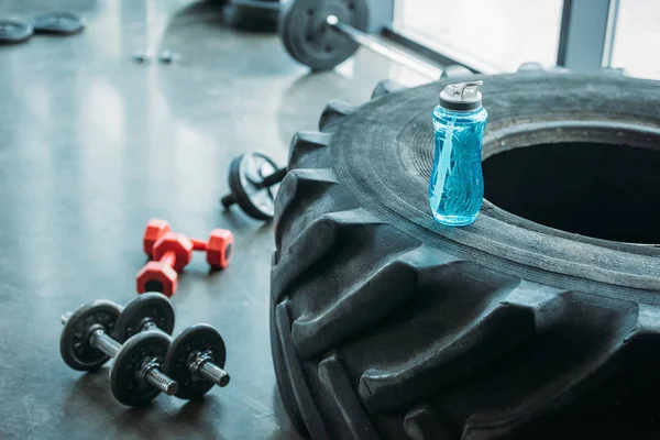 Closeup view of different dumbbells, abs roller and bottle of water on training tire at gym — Stock Photo