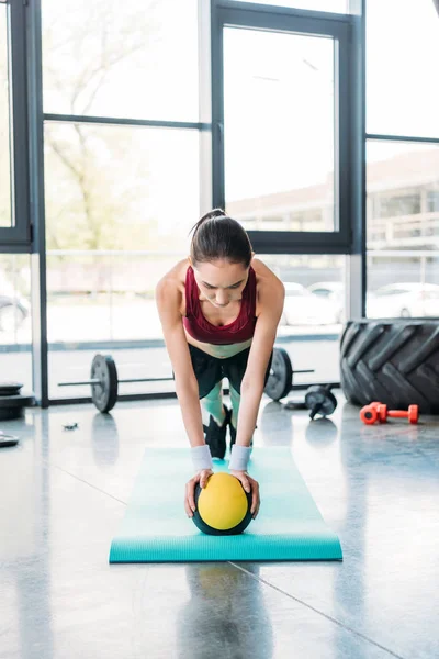 Giovane sportiva asiatica in equilibrio sulla palla sul tappeto fitness in palestra — Foto stock