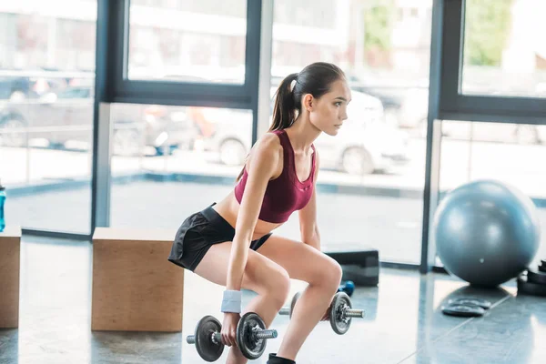 Seitenansicht einer asiatischen Sportlerin, die im Fitnessstudio mit Kurzhanteln trainiert — Stockfoto