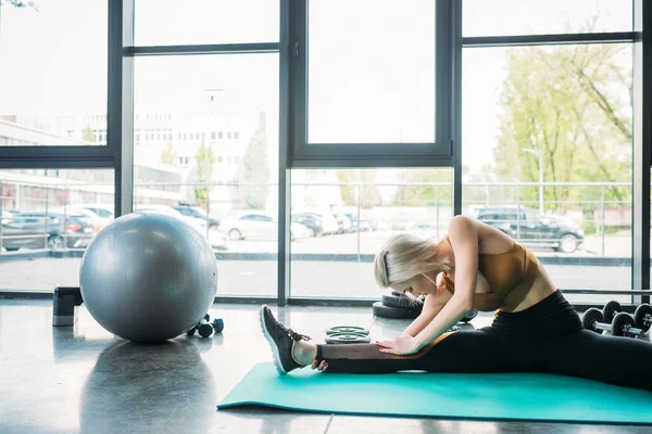 Jeune femme athlétique étirant sur tapis de fitness à la salle de gym — Photo de stock