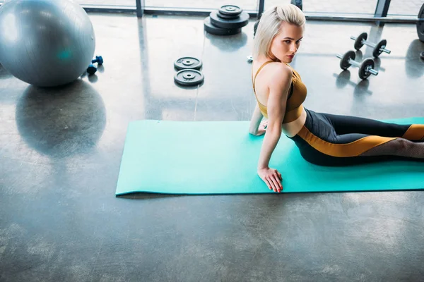 Вид сбоку молодой спортсменки отдыхающей на фитнес-коврике после тренировки в тренажерном зале — стоковое фото