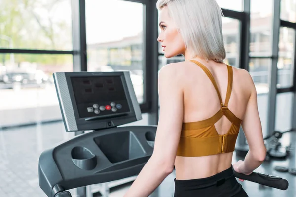 Vue arrière de la formation de la jeune sportive sur tapis roulant au gymnase — Photo de stock