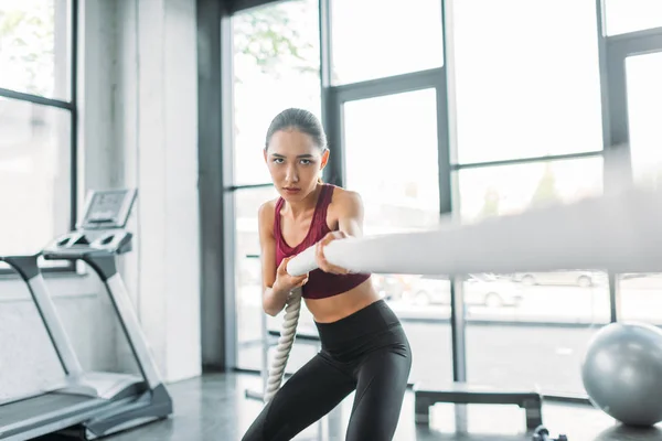 Young asian sportswoman working out with battle rope at gym — Stock Photo