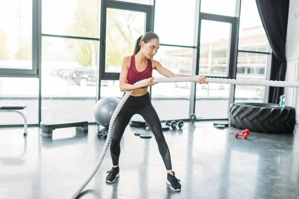 Seitenansicht einer jungen asiatischen Sportlerin, die im Fitnessstudio mit einem Kampfseil trainiert — Stockfoto