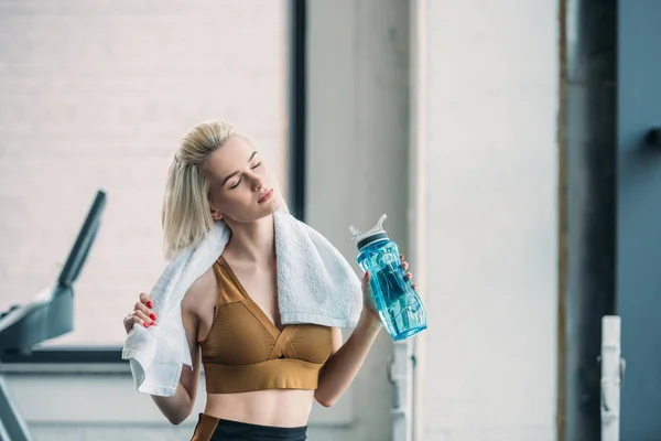 Retrato de joven deportista con botella de agua deportiva y toalla después del entrenamiento en el gimnasio - foto de stock