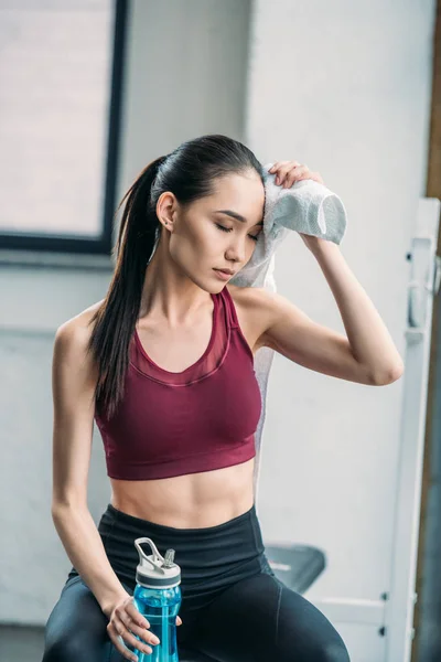 Cansada deportista asiática con toalla y botella de agua después del entrenamiento en el gimnasio - foto de stock