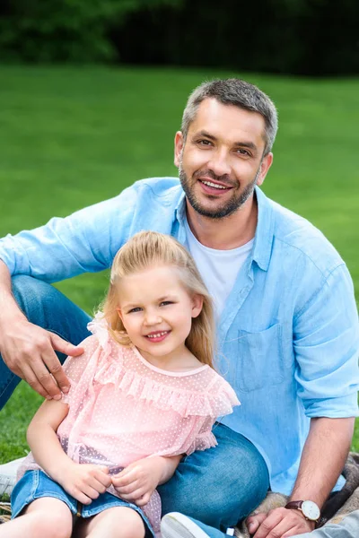 Счастливый отец с милой маленькой дочкой, улыбающейся перед камерой в парке — стоковое фото