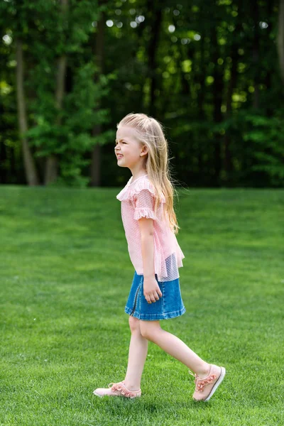 Vista lateral de un adorable niño pequeño caminando sobre hierba en el parque - foto de stock