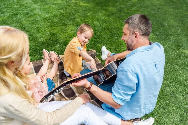 Padre feliz tocando la guitarra mientras pasa tiempo con la familia en el parque - foto de stock
