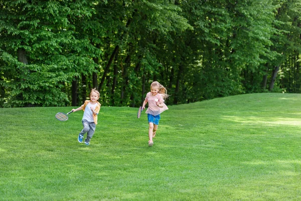 Simpatici bambini con racchette da badminton che corrono insieme nel parco — Foto stock