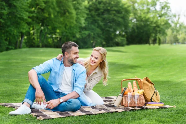 Glückliches Paar lächelt einander an, während es zusammen auf Plaid beim Picknick sitzt — Stockfoto