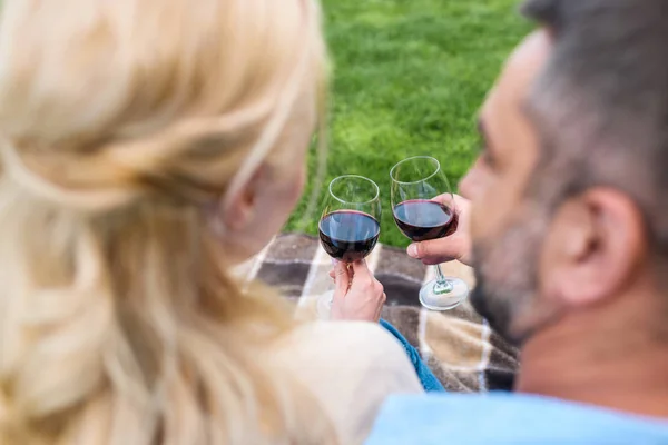 Enfoque selectivo de pareja sosteniendo vasos de vino mientras se sientan juntos en el picnic - foto de stock