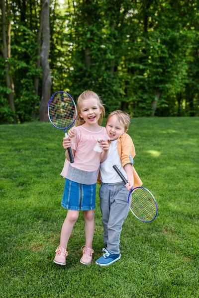 Cute happy kids holding badminton rackets and shuttlecock in park — Stock Photo