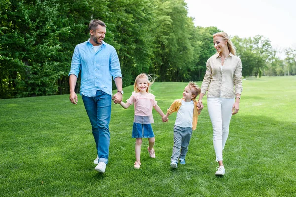Happy family holding hands and walking together in park — Stock Photo