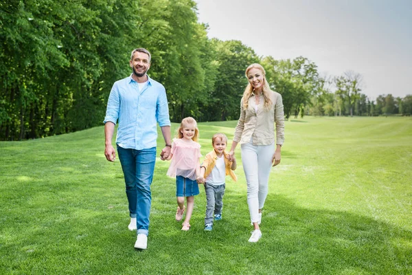 Happy family holding hands and smiling at camera while walking together in park — Stock Photo