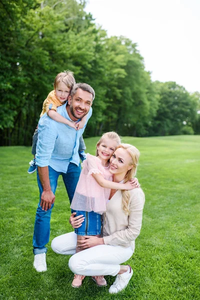 Glückliche Familie, die sich umarmt und in die Kamera lächelt, während sie Zeit miteinander im Park verbringt — Stockfoto