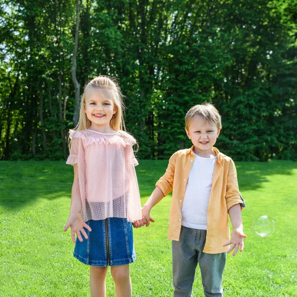 Entzückende kleine Kinder halten Händchen und lächeln in die Kamera im Park — Stockfoto