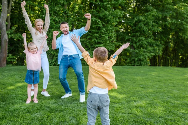 Alegre familia levantando las manos y sonriendo unos a otros en el parque - foto de stock