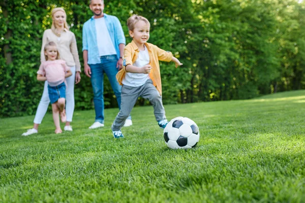 Family looking at little boy playing with soccer ball in park — Stock Photo