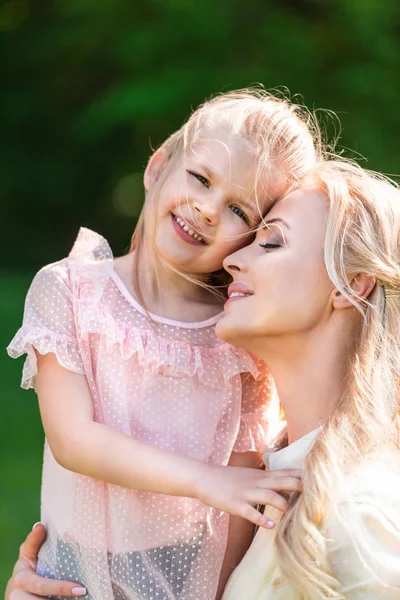 Feliz madre e hija abrazando y sonriendo en el parque - foto de stock