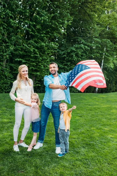 Família feliz com duas crianças segurando bandeira americana no parque — Fotografia de Stock