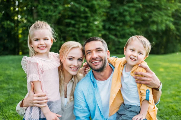 Famiglia felice con due bambini sorridenti alla macchina fotografica insieme nel parco — Foto stock