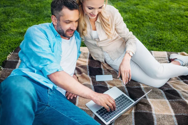 High angle view of smiling couple using laptop on plaid in park — Stock Photo