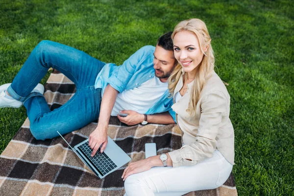 Visão de alto ângulo de casal feliz descansando em xadrez e usando laptop no parque — Fotografia de Stock
